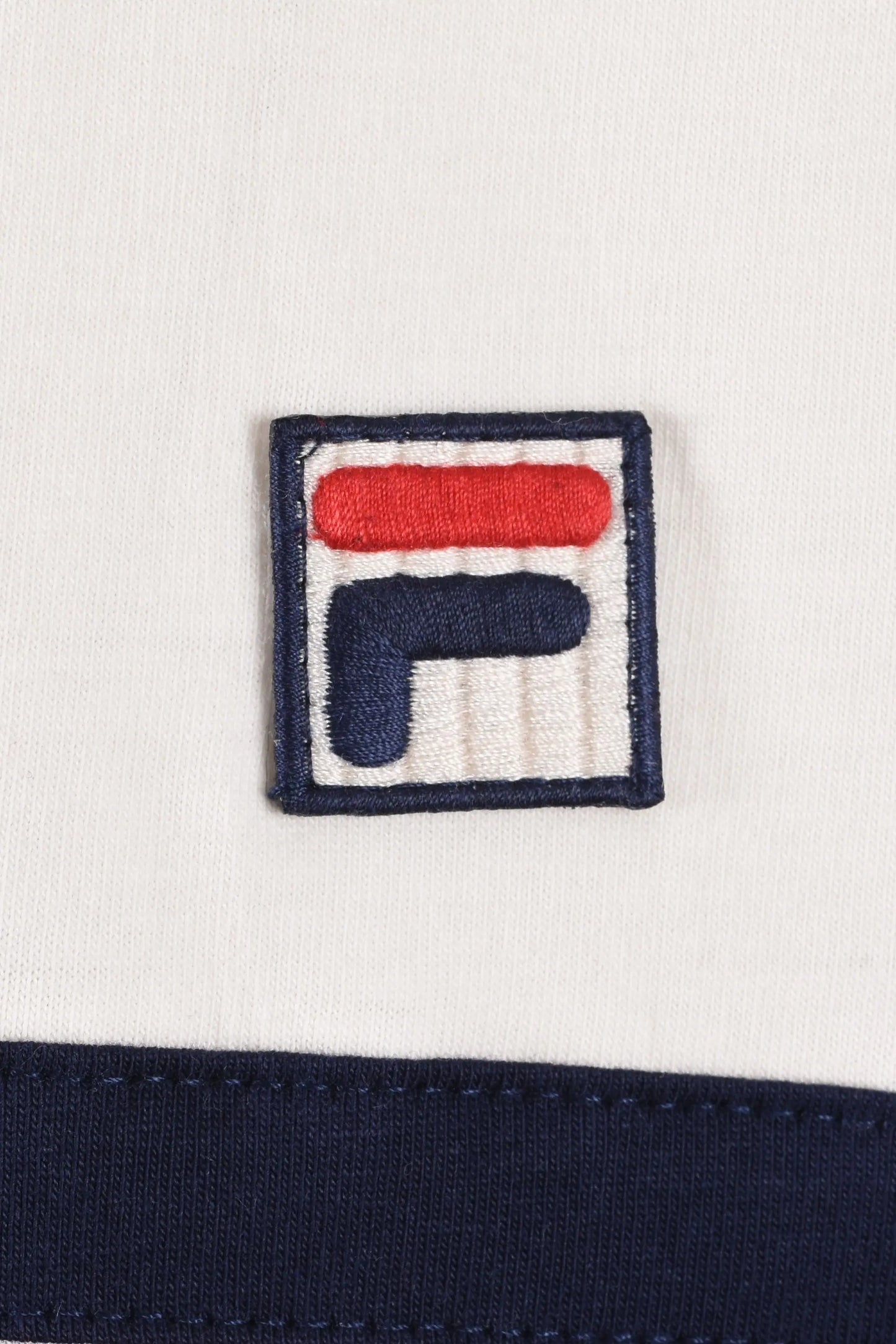 Close up of the Fila logo embraided on fabric with a gardenia background