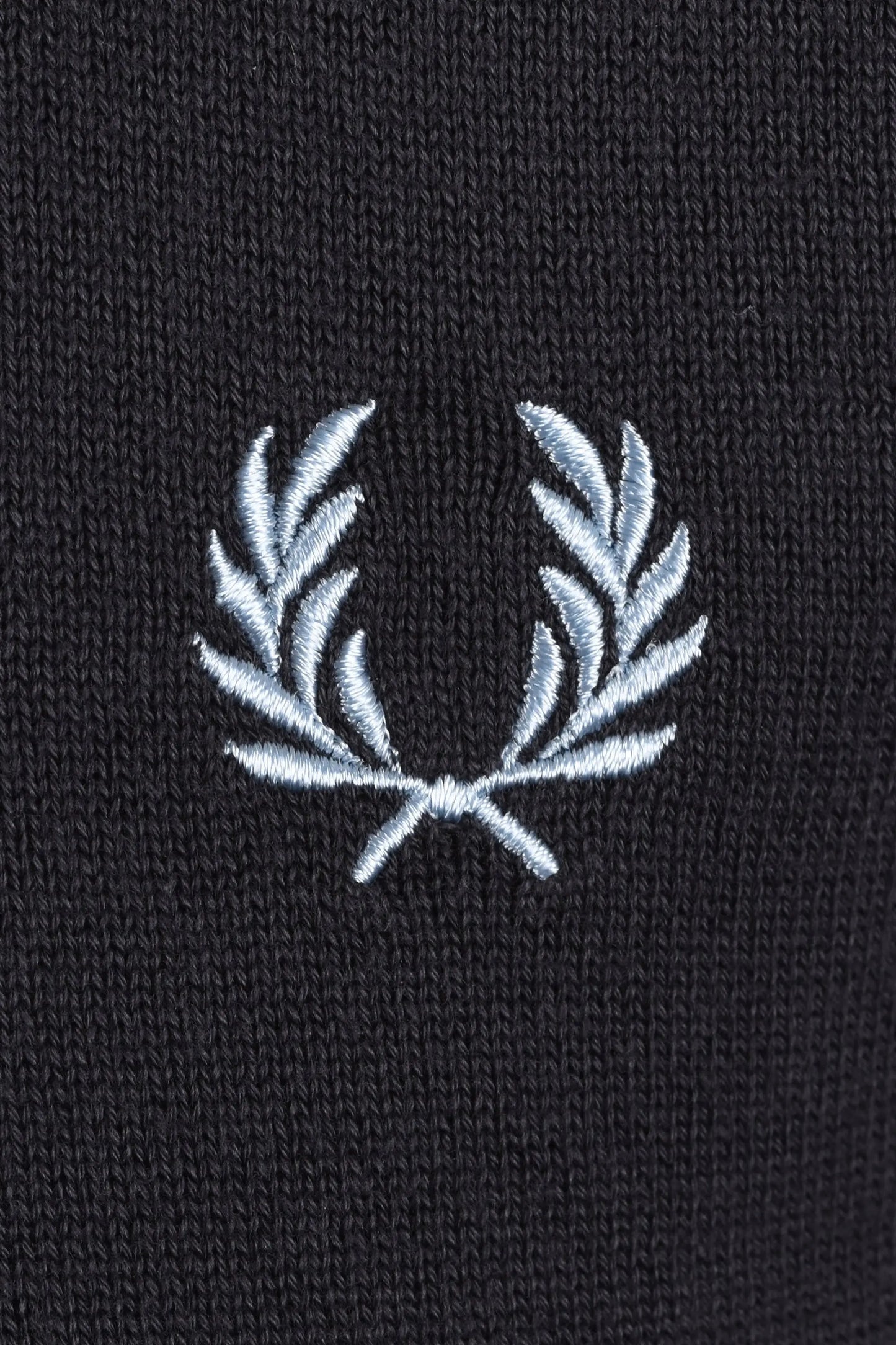 Close-up of a grey t-shirt with a white embroidered fred perry logo on a dark background