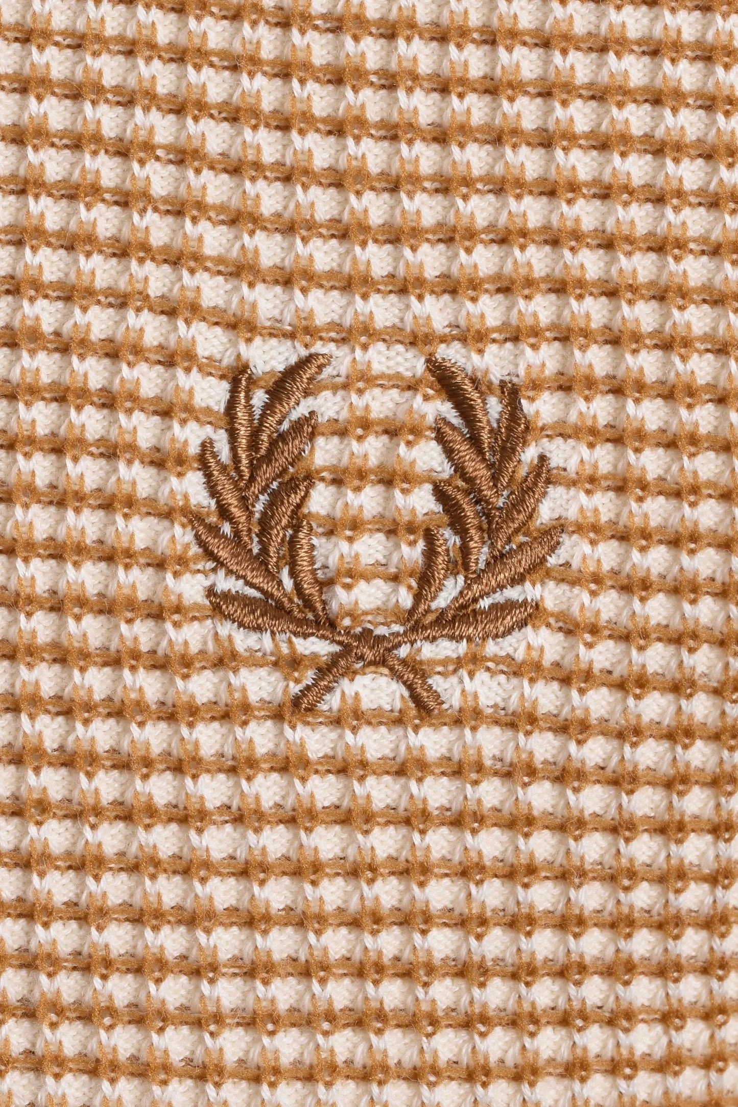 Close up of the Fred Perry laurel wreath logo embroidered on a textured waffle knit fabric in the colour tonic.