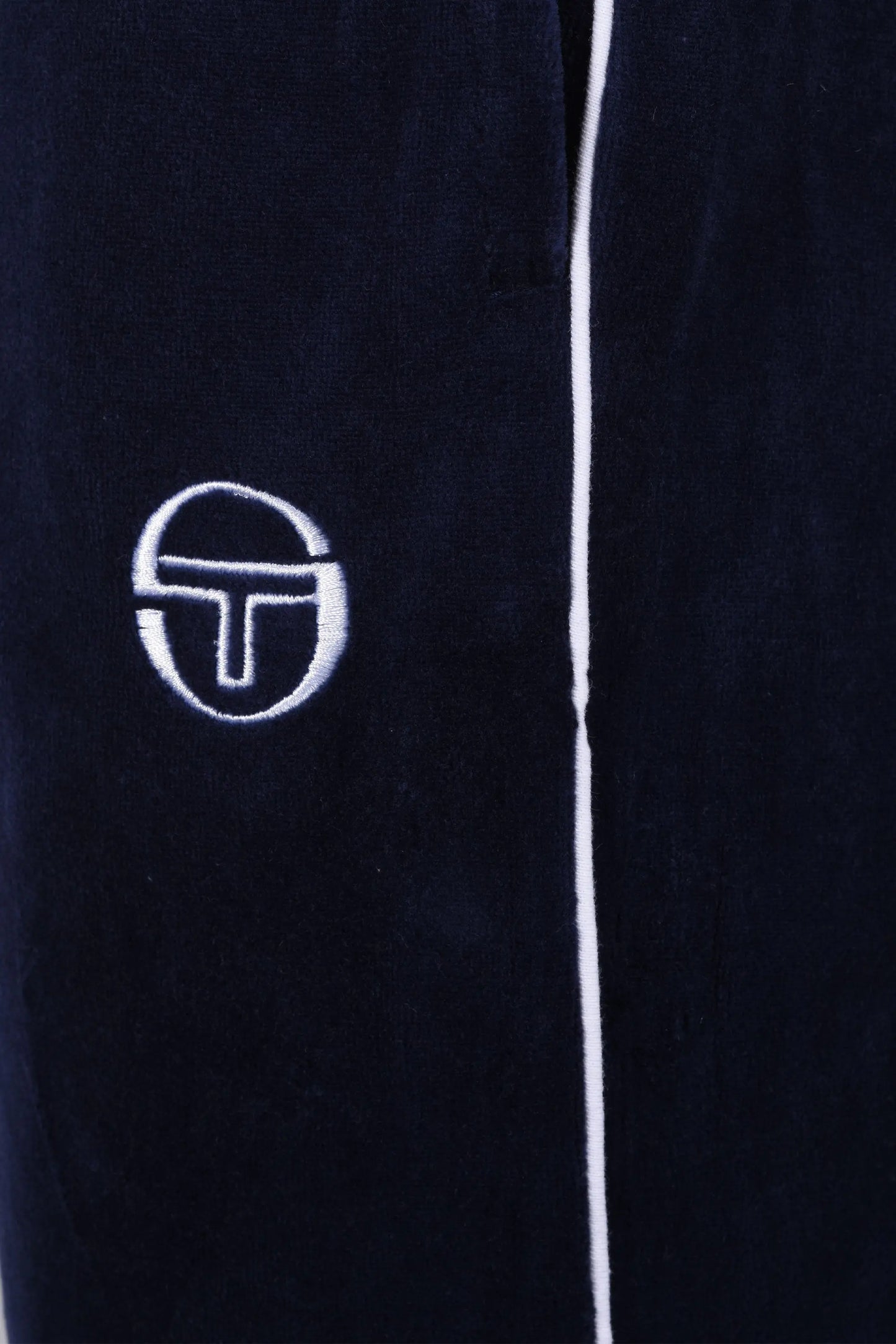 Close up of the white embroidered logo on a pair of Sergio Tacchini Tasso velour trackpants in navy blue