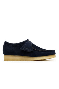 Side profile picture of the Clarks originals wallabee shoes in the colour navy, shows the Clarks originals branded swing tag as well as the rubber wedge sole.