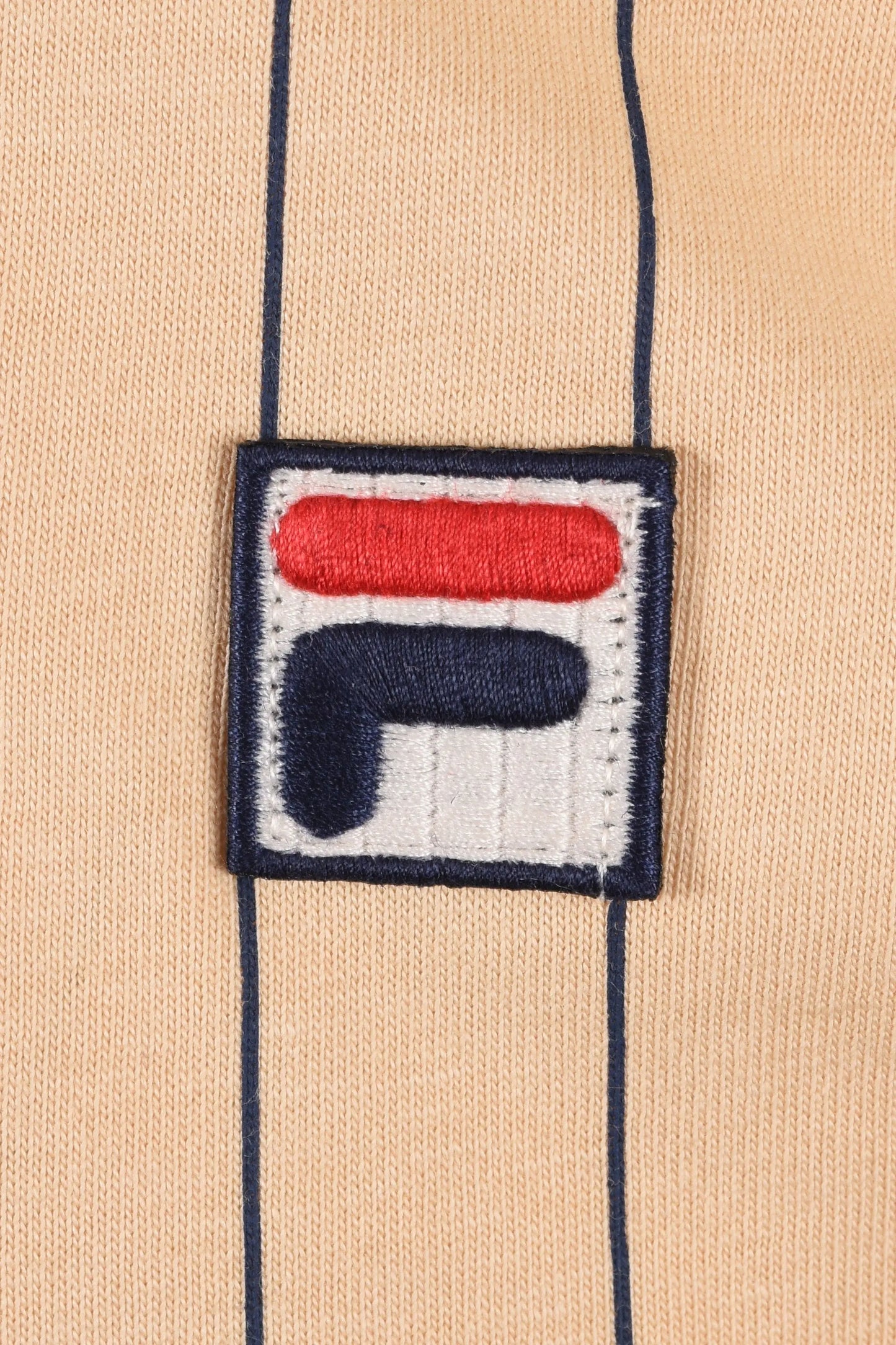 Close up of the Fila embroidered logo upon a neutral stripe background