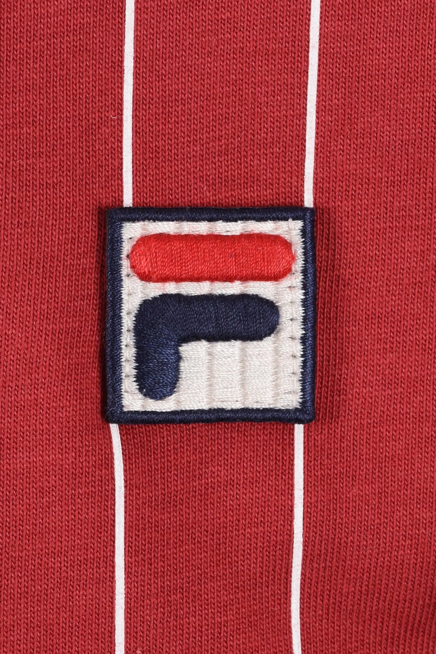 Close up of an embroidered Fila logo on a red background with white stripes