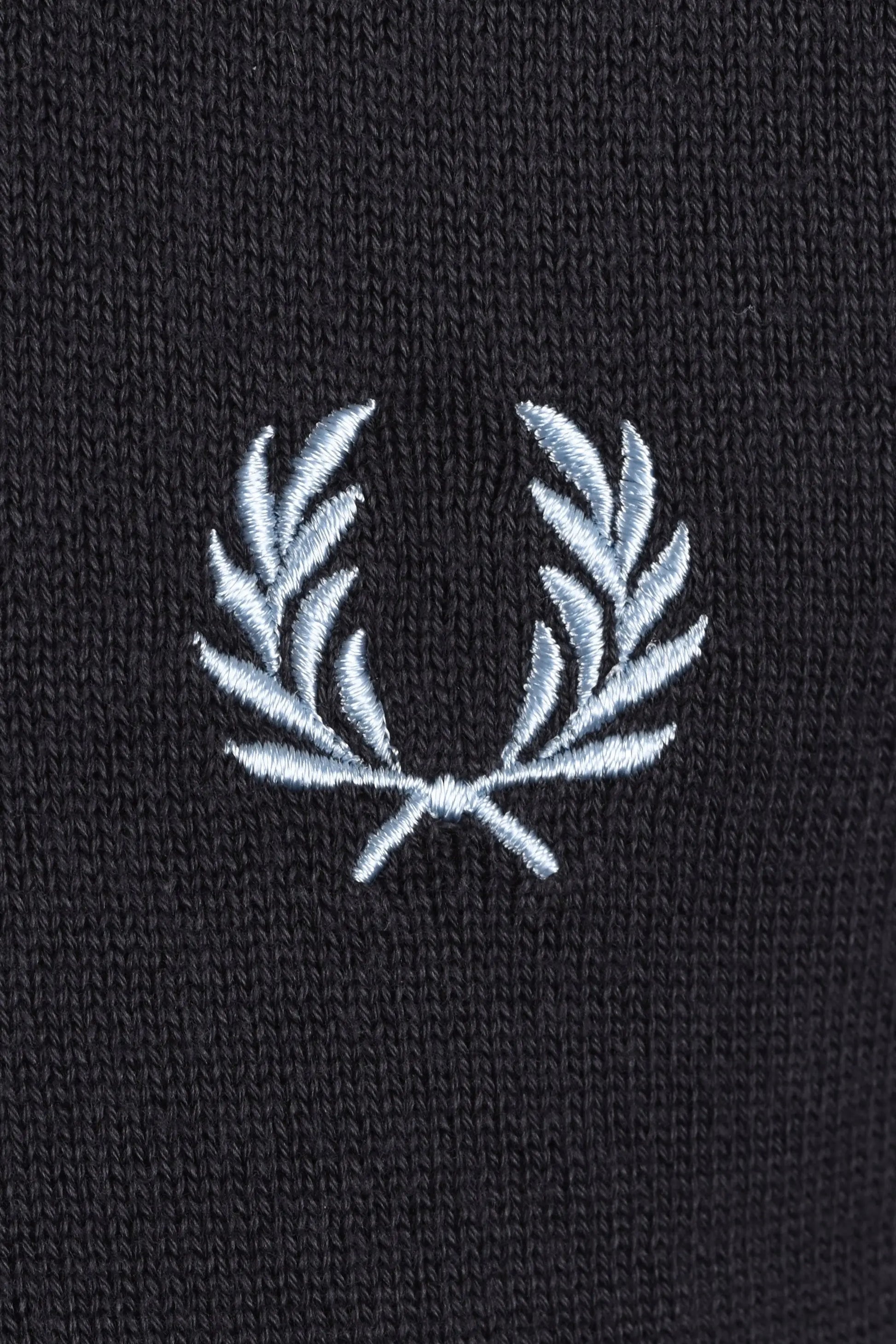 Close-up of a grey t-shirt with a white embroidered fred perry logo on a dark background