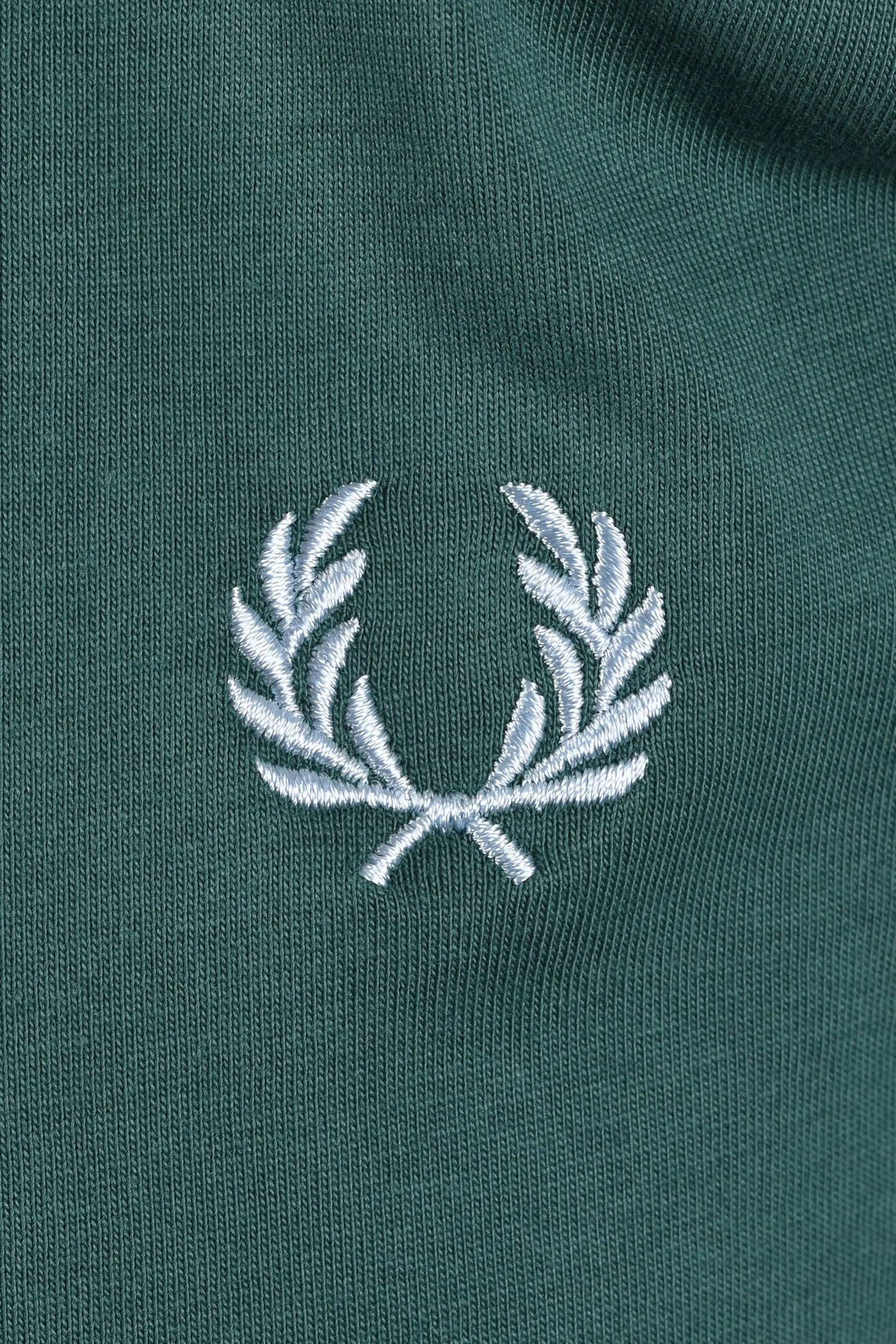 Close-up of a green polo shirt with a light blue embroidered fred perry logo 
