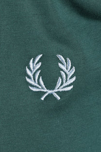 Close-up of a green polo shirt with a light blue embroidered fred perry logo 