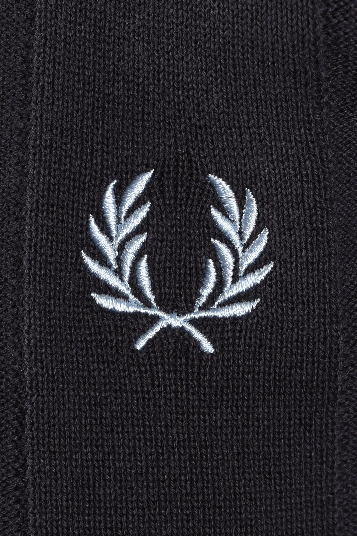 Close-up of a light blue embroidered fred perry logo on a dark grey polo