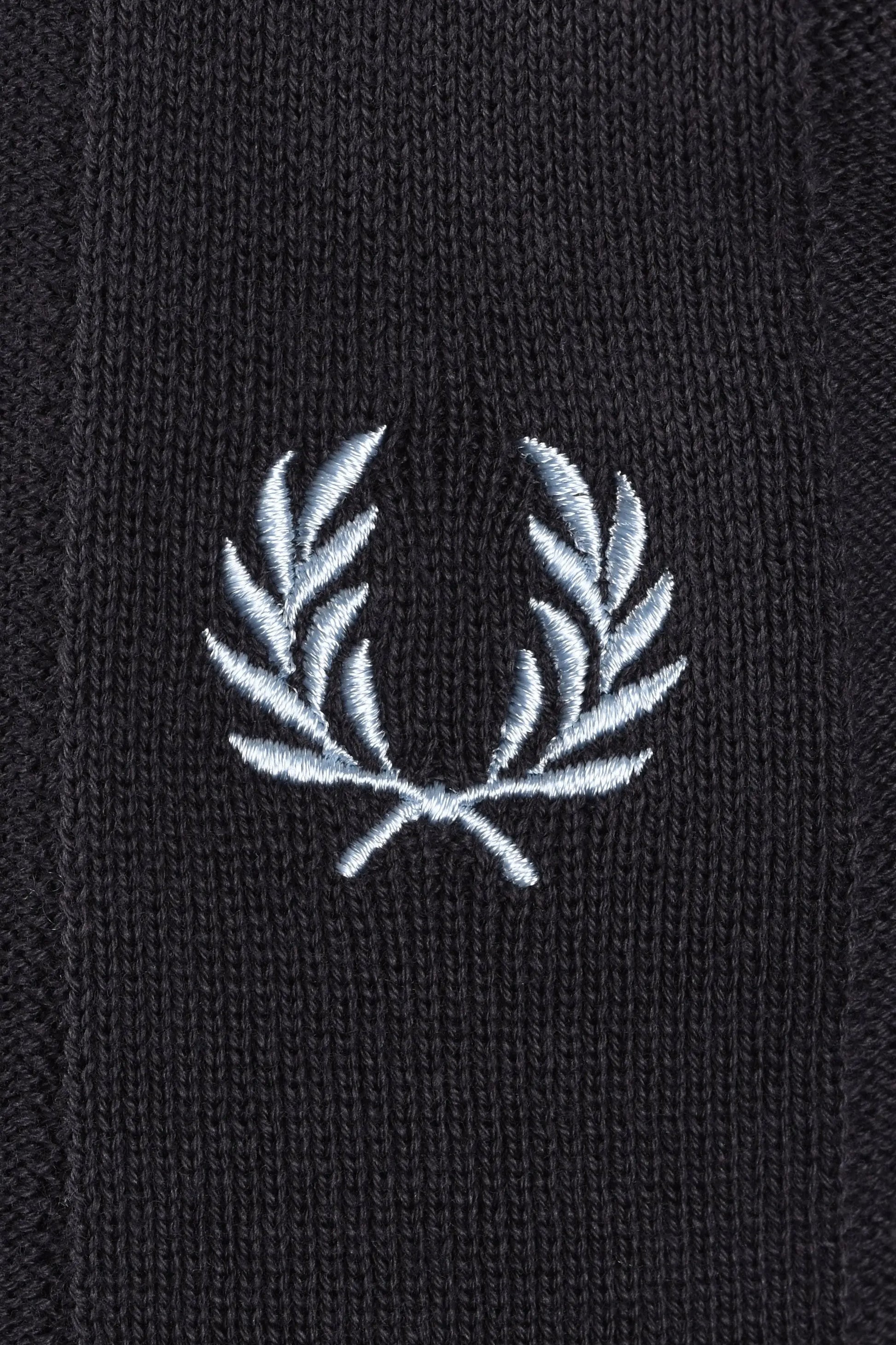 Close-up of a light blue embroidered fred perry logo on a dark grey polo