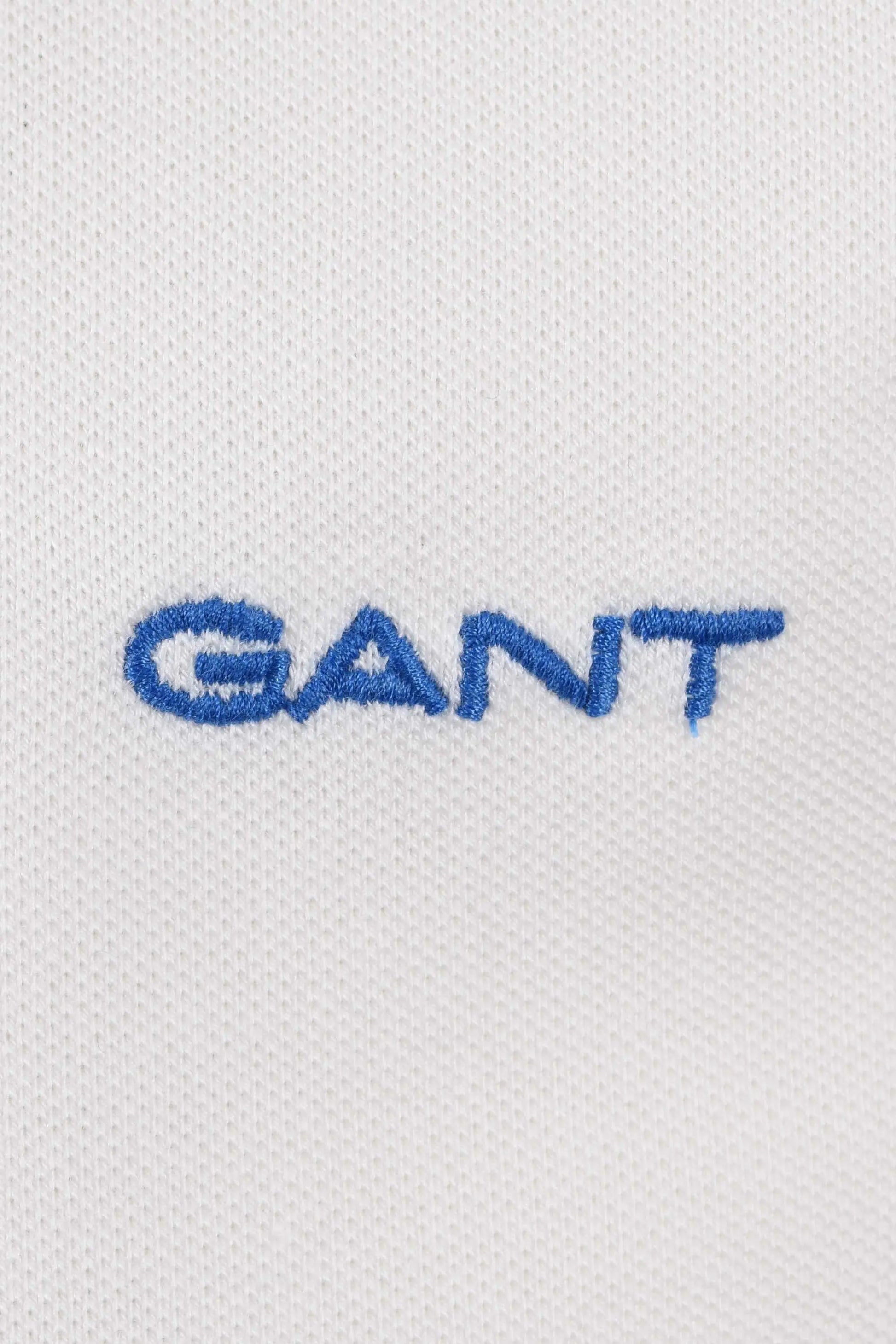 Close up of the Gant embroidered logo in blue upon a white textured background.