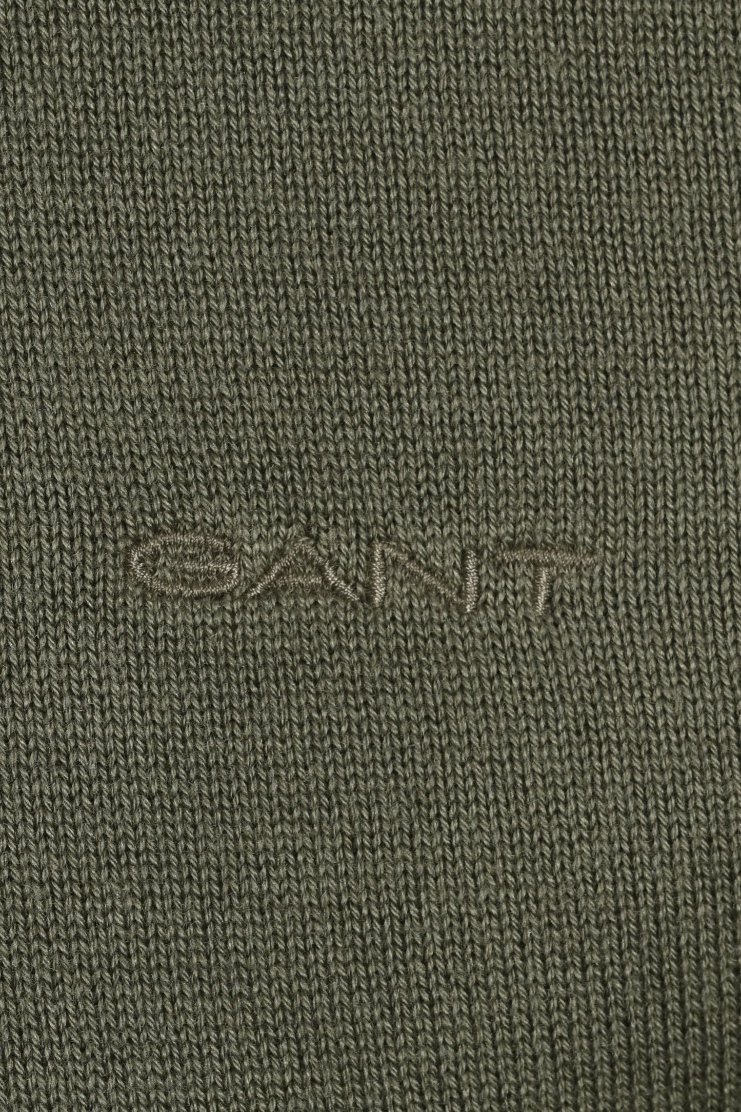 Close up of the embroidered Gant logo on a knitted material all in a dry herb green colour.