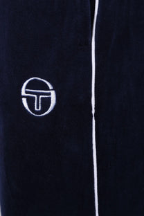 Close up of the white embroidered logo on a pair of Sergio Tacchini Tasso velour trackpants in navy blue