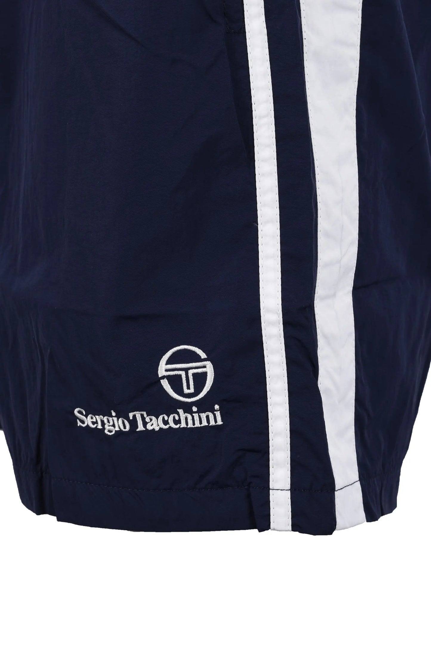 Bottom of the leg of a pair of Sergio Tacchini shorts in navy showing the Sergio Tacchini logo in white as well as a twin side stripe down the side of the leg of the shorts.