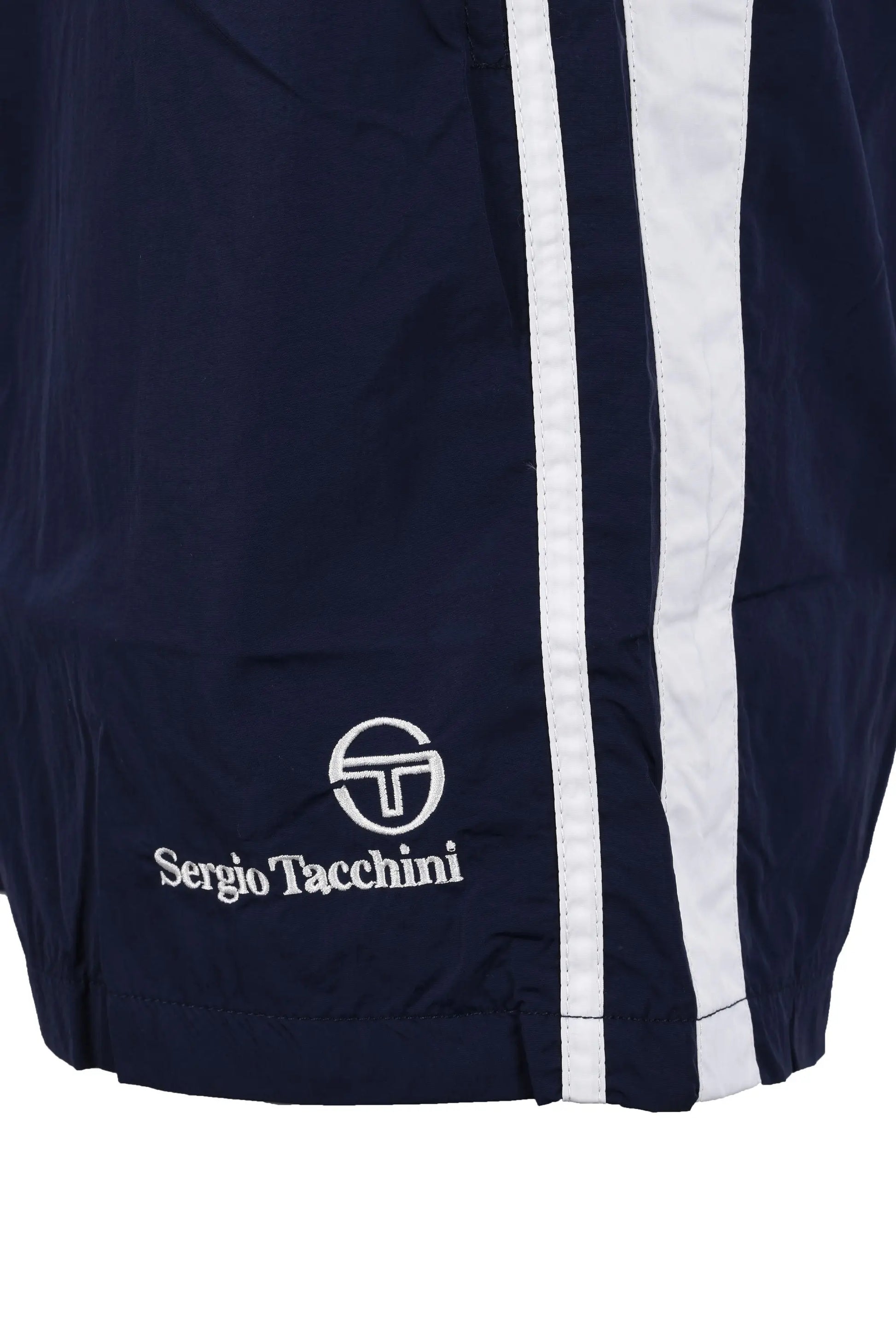 Bottom of the leg of a pair of Sergio Tacchini shorts in navy showing the Sergio Tacchini logo in white as well as a twin side stripe down the side of the leg of the shorts.