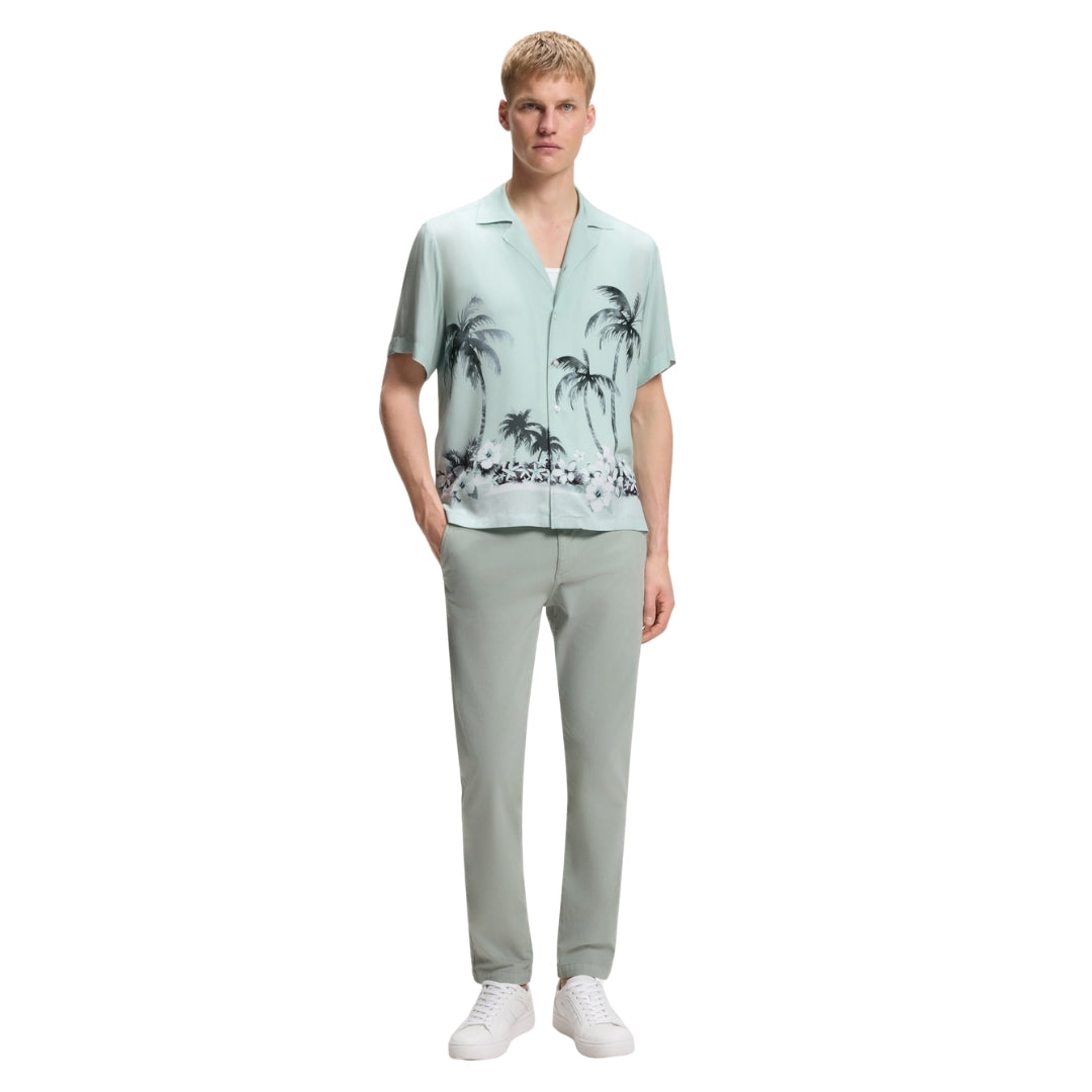 Man wearing a light green BOSS shirt with palm tree design and light gray pants on a white background